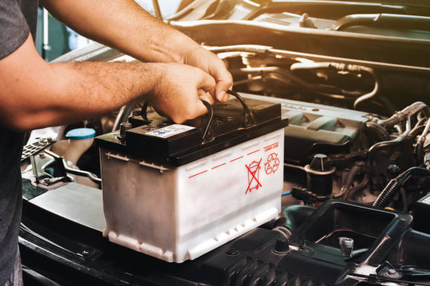 A auto mechanic carries a replacement car battery for car electrical maintenance in the auto repair garage